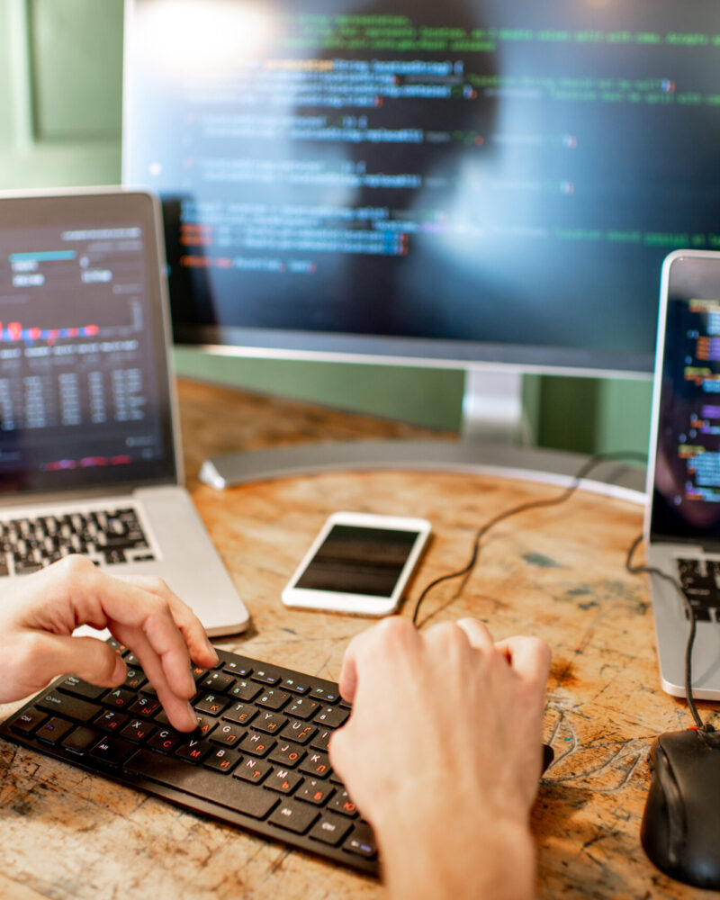 Programmer working with program code Young programmer writing a program code sitting at the workplace with three monitors in the office